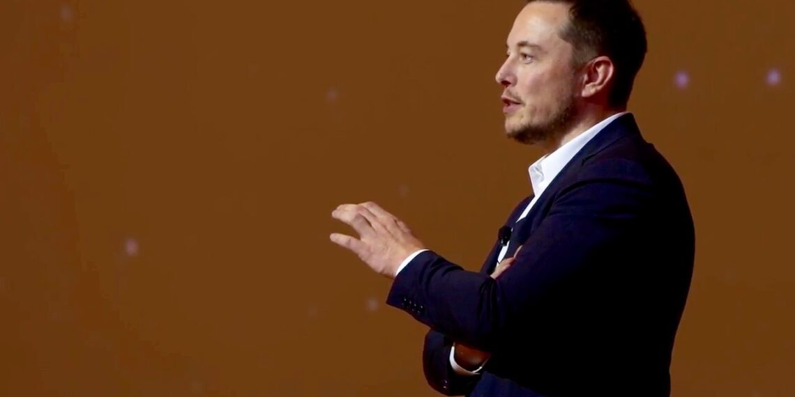 Elon Musk discursando em palestra em pé